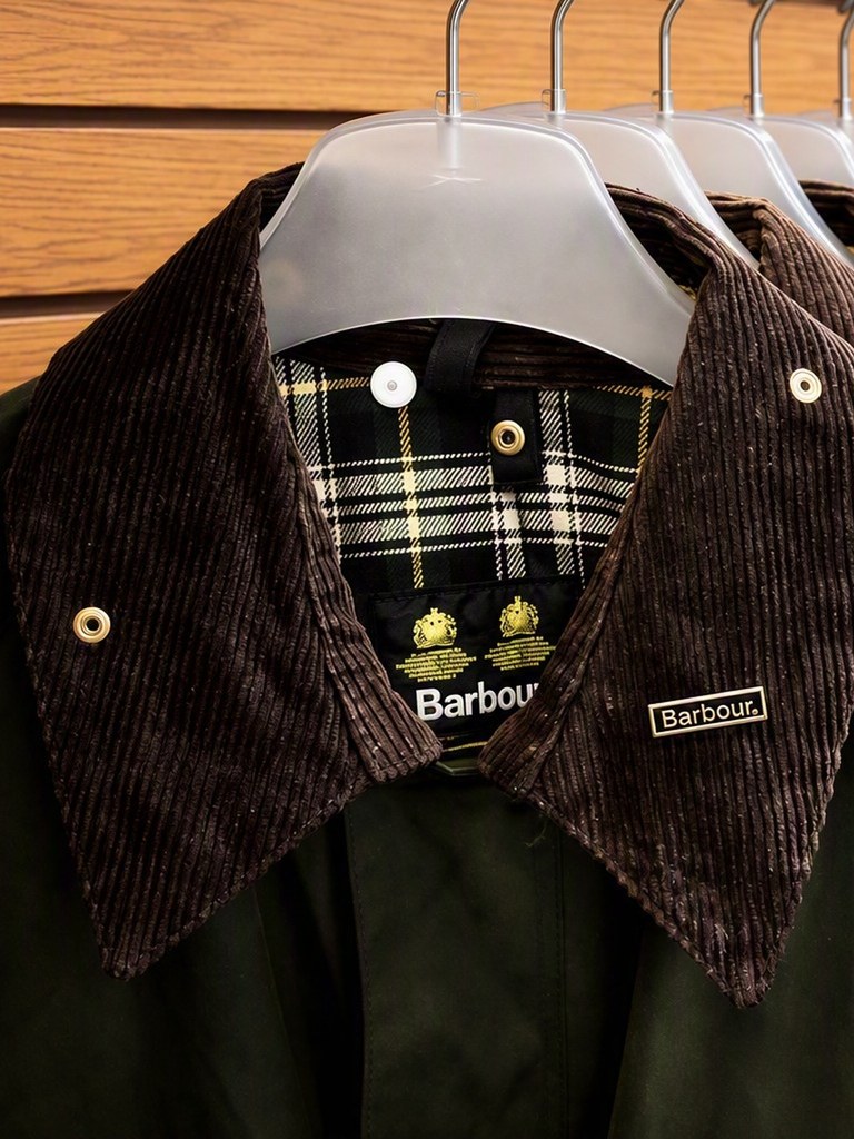 Barbour wax jacket with brown corduroy collar and tartan lining on the rail at The Gun Cupboard
